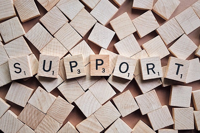 Scrabble tiles spread across surface with some aligned to spell the word "Support".