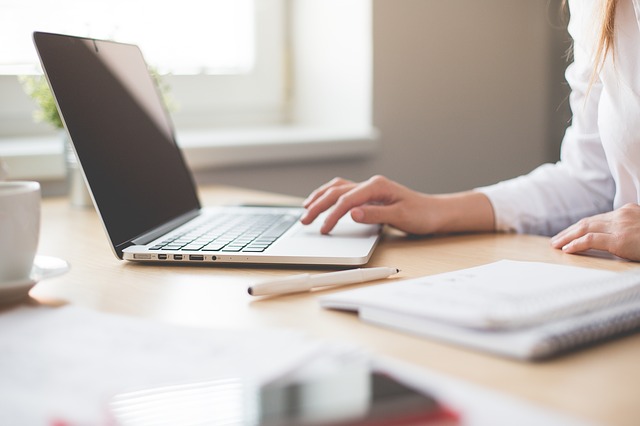 Woman typing on laptop with notepad and pencil on desk